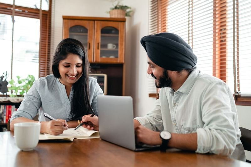 Two colleagues smiling while reviewing notes and a laptop together at a wooden table