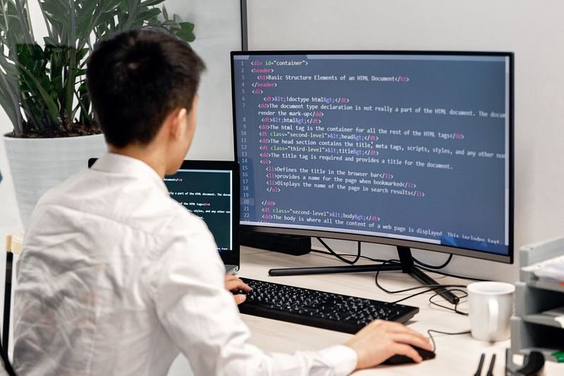 Over-the-shoulder view of a developer writing HTML code on a large curved monitor