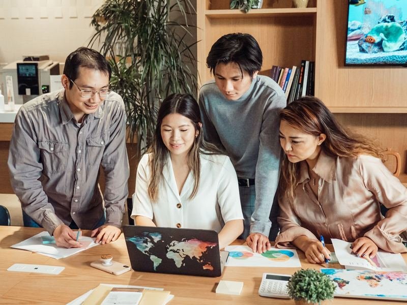 Four colleagues working together around a laptop and printed charts at a meeting table